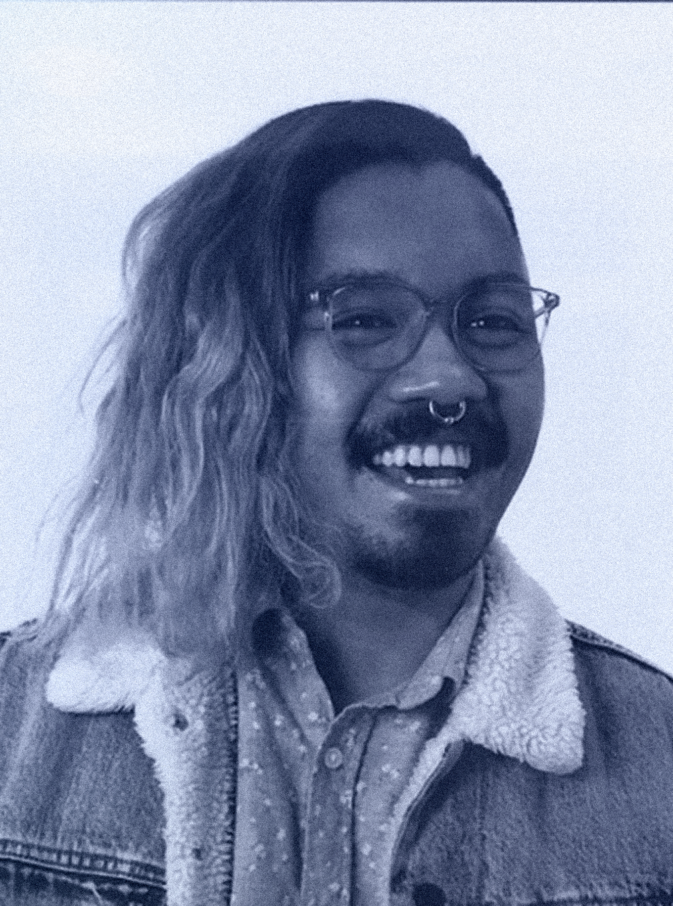 A picture of me with a big goofy grin. Long hair swept to the side. Glasses and a septum piercing.